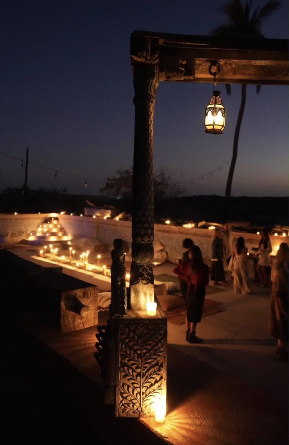 Candlelit terrace at dusk with a carved wooden column and a hanging lantern