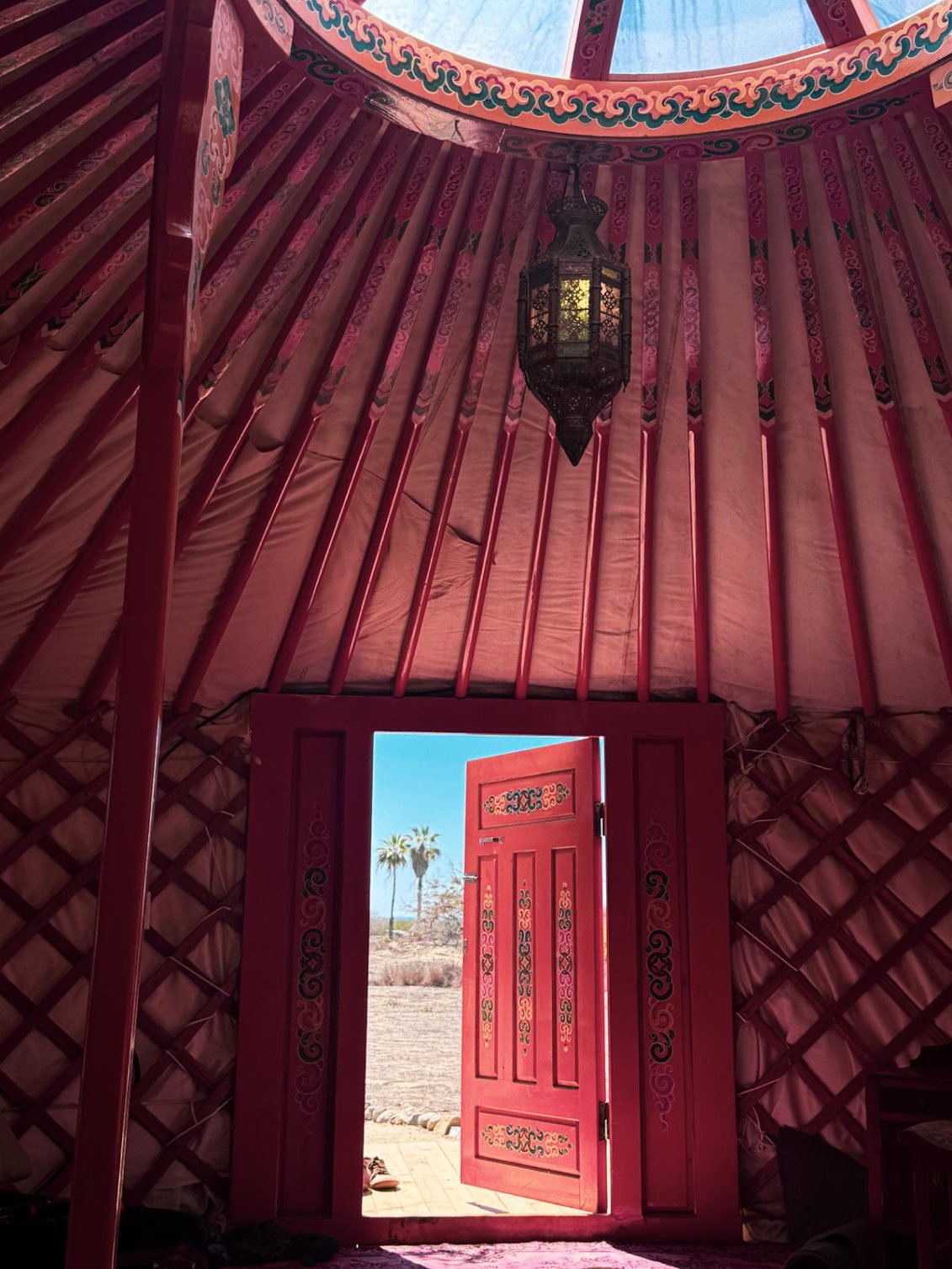 Inside a painted red yurt, looking out the open door toward palm trees