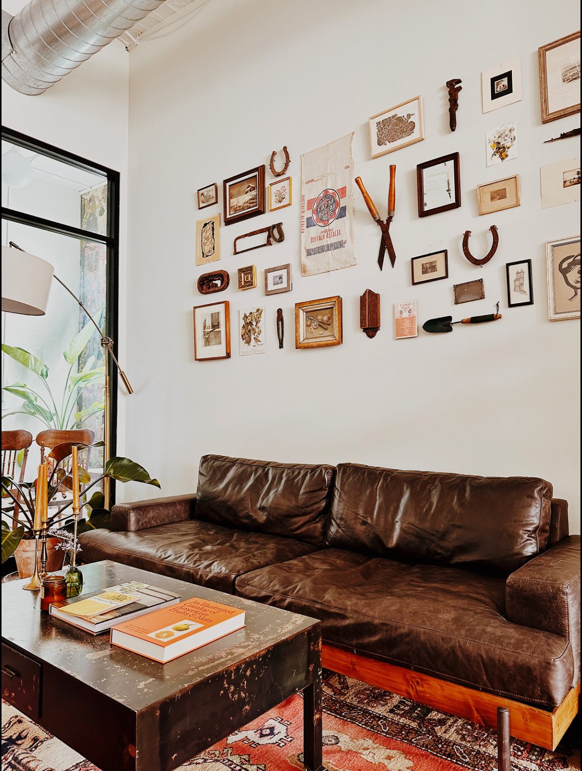 Dark leather sofa beneath a gallery wall of framed prints and vintage tools