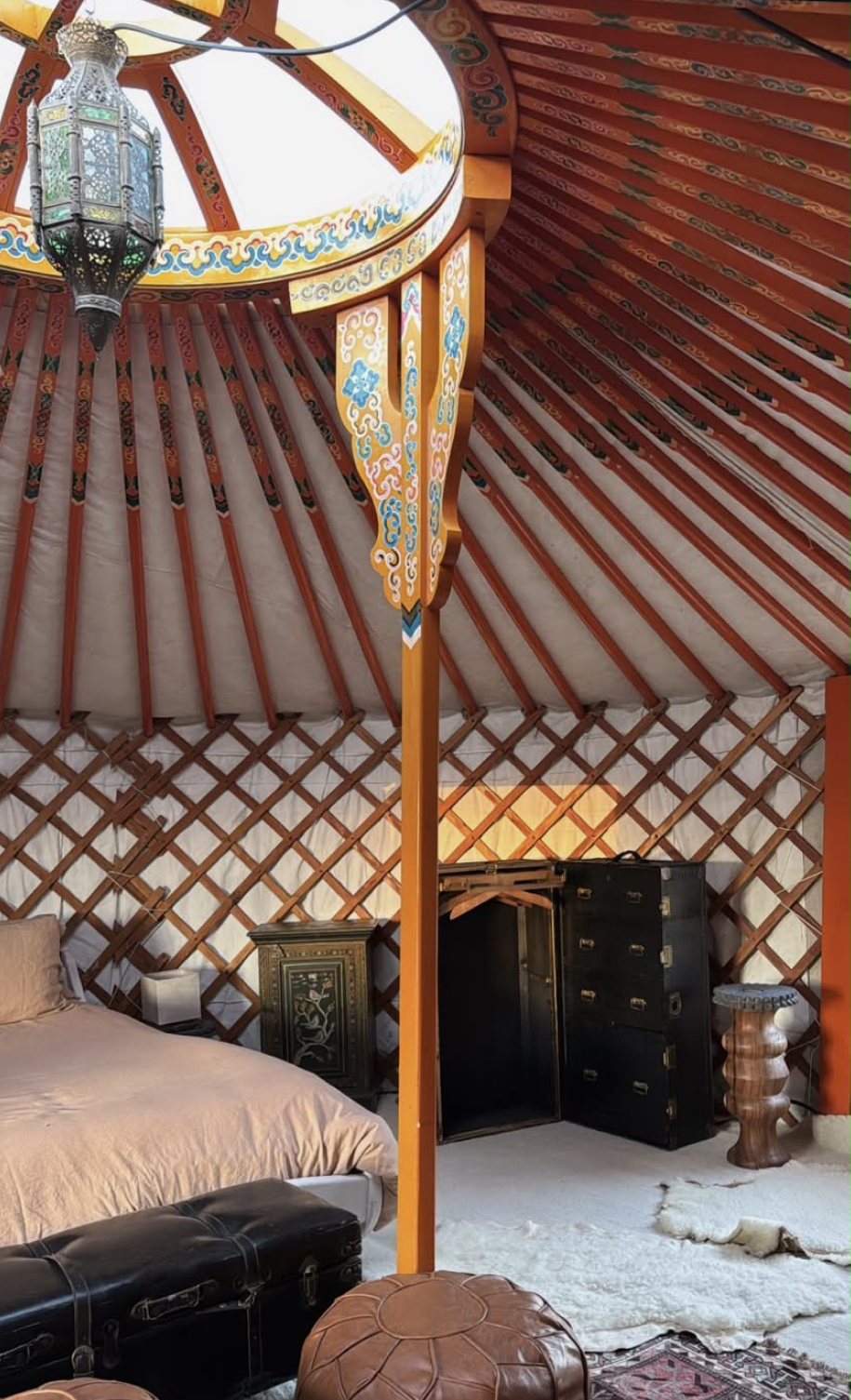 Yurt bedroom with an orange painted center pole, lattice walls and a hanging lantern